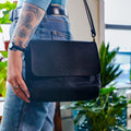 A woman carrying a shoulder bag made from black waxed canvas and leather.